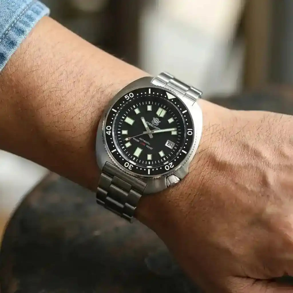 Relógio Automático Masculino Marinor Black sendo usado no pulso sobre mesa evidenciando o mostrador preto de 44mm e o bezel cerâmico unidirecional